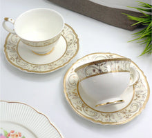 Load image into Gallery viewer, Set of white ceramic tea cups and saucers with gold detailing on a white surface.
